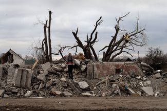 Местная жительница ищет свои вещи на развалинах разрушенного жилого дома, ей помогают пожарные