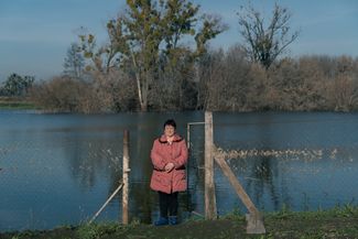 Svitlana Marchenko stands at the edge of her garden, which now backs onto a flooded field. The debris on the chainlink fence shows how high the water level was earlier this year.