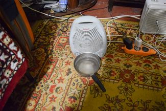 A space heater and a pot of water sits on the floor of the cramped apartment. Lyuda uses this makeshift humidifier to add moisture to the air. Kostiantynivka, November 2023.