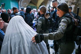 Сотрудница израильских сил безопасности разговаривает с мусульманками, прибывшими в Старый город Иерусалима на пятничную молитву. 13 октября 2023 года