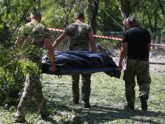 Судмедэксперты уносят тело жертвы авиаудара с места происшествия