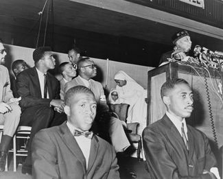 Лидер «Нации ислама» Элайджа Мухаммад выступает перед своими последователями, среди которых боксер Мухаммед Али (второй справа в верхнем ряду). 1964 год