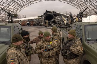 Служащие ВСУ на фоне пикапов с легкими зенитными пулеметами и разрушенного самолета «Мрия» в аэропорту Антонов под Киевом