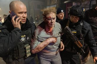Украинские полицейские сопровождают раненую жительницу Харькова после российского ракетного удара по жилому дому в центре города