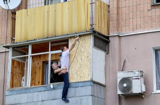 Жители Харькова ремонтируют балкон после ракетного удара по микрорайону Пятихатки. Обстрелом разрушены окна, два этажа жилого дома и крыша соседнего. От удара пострадали и припаркованные во дворе автомобили