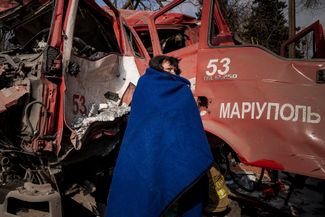 Жительница Мариуполя кутается в одеяло у уничтоженной во время обстрела пожарной машины. Российские войска вошли в Мариуполь 2 марта — город до сих пор остается под оккупацией. 10 марта 2022 года