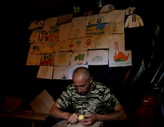 Украинский солдат чистит картошку. На стене — рисунки, которые дети передали военнослужащим, живущим в траншеях