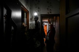 Женщина держит лампу, осматривая получивший повреждения после обстрела дом