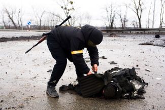 Украинский военный снимает бронежилет с тела российского бойца. Фото сделано в районе села Ситняки в Киевской области.