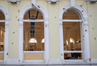 Рабочий заменяет разбитые стекла в окне здания вокзала в Херсоне после атаки российских беспилотников