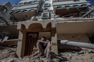 Палестинский мальчик сидит на обломках своего дома, разрушенного после израильского авиаудара по городу Газа. 13 мая 2021 года