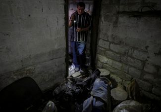 Житель Каменки Юрий Здоровец осматривает тело соседа, убитого во время обстрела со стороны России