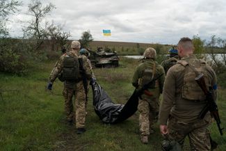 Украинские военные в только что освобожденной Харьковской области несут тело погибшего