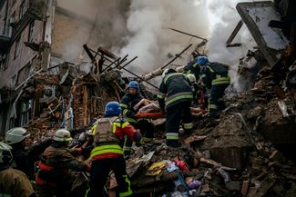 Пожарные несут тело мирного жителя, найденное под завалами одного из жилых домов
