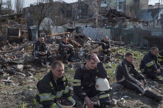 Пожарные присели передохнуть после работы на месте разрушенных из-за российских обстрелов зданий в Бородянке, Киевская область