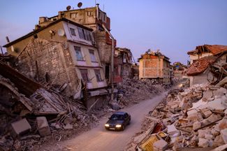 Автомобиль едет мимо разрушенных зданий в Антакье — одном из самых пострадавших от землетрясения городов Турции. Часть зданий рухнула целиком, другие пошли трещинами, покосились или сложились гармошкой. На юге Турции в результате землетрясения, произошедшего 6 февраля, погибли более 50,5 тысячи человек в 11 провинциях, были повреждены сотни тысяч зданий. В соседней Сирии во время землетрясения погибли около 8,5 тысячи человек
