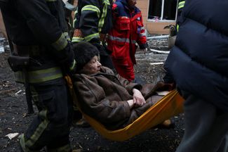 Спасатели и местный житель несут женщину, раненную в результате атаки на жилой дом