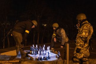 Ukrainian territorial defense fighters guard the barricades in eastern Kyiv, passing the time by playing checkers with some Molotov cocktails