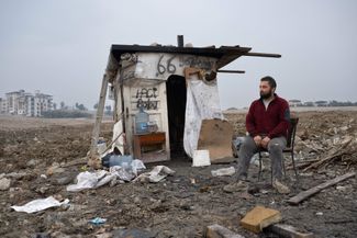 Мужчина сидит рядом с импровизированной хижиной, в которой вынужден спасаться от непогоды. Его дом был разрушен год назад в результате землетрясения