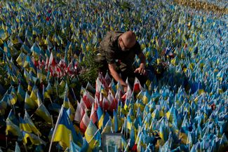 Ветеран армии Польши Славомир Высоцкий устанавливает флаг своей страны на мемориале в Киеве в честь польского фельдшера, погибшего на полномасштабной войне России и Украины