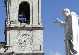 Статуя Святого Бенедикта на фоне разрушенной колокольни городской ратуши в Норче