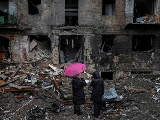 Жители Вышгорода Киевской области стоят возле своего дома, разрушенного российским ракетным обстрелом, нанесенным 23 ноября. По данным украинских властей, под обстрел попали два жилых дома. Погибли шесть человек, еще 30 пострадали