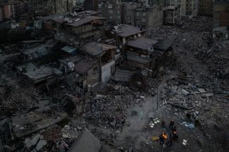 Работники службы экстренной помощи греются у огня среди обломков разрушенных зданий в провинции Хатай на юге Турции