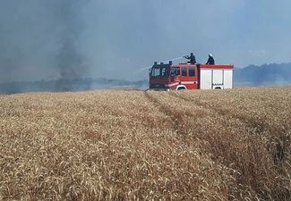 Украинские пожарные тушат огонь на пшеничном поле, возникший после обстрела Николаевской области. Города и села области, в которой сейчас идет уборка урожая пшеницы, регулярно подвергаются обстрелам со стороны России