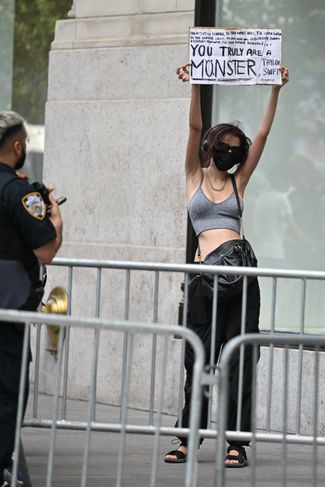 A protester stands holding a sign criticizing Taylor Swift. Poster says: 