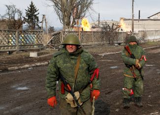 Combatants in pro-Russian militia units patrol Volnovakha’s streets. Behind them, fires fed by broken gas pipes burn.