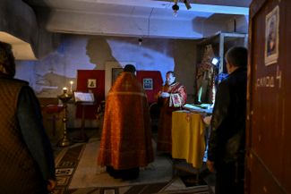 Православные священники молятся с жителями во временной подвальной церкви в Лисичанске 20 мая 2022 года. Неподалеку от города в последние недели проходят одни из самых активных боев на фронте