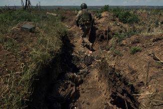 Украинский солдат входит в недавно захваченную траншею, где остаются тела российских военных