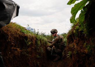 Украинский военнослужащий с позывным «Тихий» осматривает окрестности из окопа менее чем в километре от линии фронта