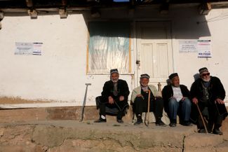 Local residents sit in front of a sign promoting the constitutional referendum in southern Uzbekistan