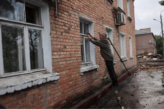 Местный житель пытается починить разбитое в результате обстрела окно