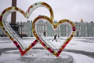 Российский солдат бежит мимо инсталляции с изображением двух сердец. На них написано «Санкт-Петербург и Мариуполь». 12 декабря 2022 года