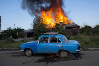 Житель Бахмута едет мимо горящего дома на окраине города