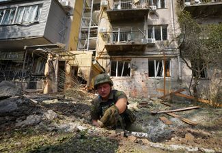 Украинский военнослужащий собирает осколки снаряда в воронке, образовавшейся после удара, чтобы определить тип боеприпаса, выпущенного по жилому району города