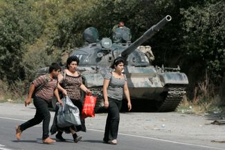 Georgian refugees walk past a Russian armored vehicle in the village of Igoeti. Georgia, August 16, 2008.
