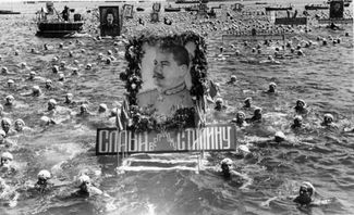 Soviet sailors swimming alongside floats with portraits of Joseph Stalin in celebration of Navy Day. Sevastopol, USSR. July 1950.