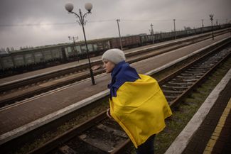 Жительница Херсона, закутанная в украинский флаг, ждет поезд из Киева, на котором к ней возвращается дочь