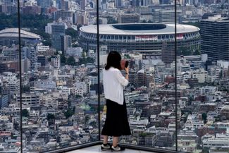 Женщина делает фото на смотровой площадке с видом на Национальный олимпийский стадион в Токио, 10 июля 2021 года.
