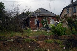Мужчина чинит крышу дома в селе Русская Лозовая. Во дворе перед его домом — траншеи