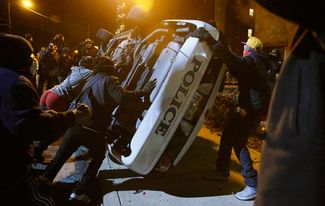 Митингующие переворачивают полицейскую машину в Фергюсоне после того, как суд оправдал полицейского, застрелившего афро-американского тинейджера, 25 ноября 2014 года