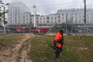 Работник муниципальных служб убирает мусор у жилого дома, пострадавшего от российского ракетного удара