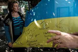 58-летняя жительница села Троицкое показывает украинский флаг, который она сохранила в своем доме во время российской оккупации. Автографы на флаге оставили освободившие село военные ВСУ