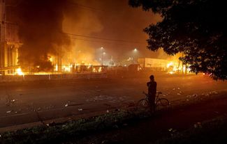 Демонстранты смотрят на зарево пожаров от горящих зданий. Миннеаполис, штат Миннесота, 27 мая 2020 года