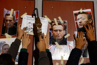 Люди вешают портреты Алексея Навального у главных ворот российского посольства в мальтийской Каппаре во время акции протеста. 19 февраля 2024 года