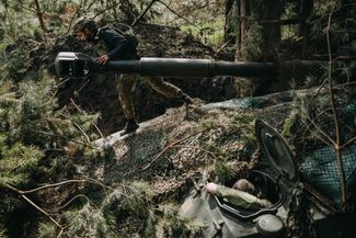 Боец украинской 63-й бригады маскирует самоходную гаубицу «Акация» в лесу