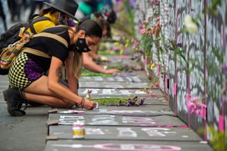 Участница марша в Мехико пишет на заборе, выставленном вокруг Национального дворца, имена жертв фемицида.